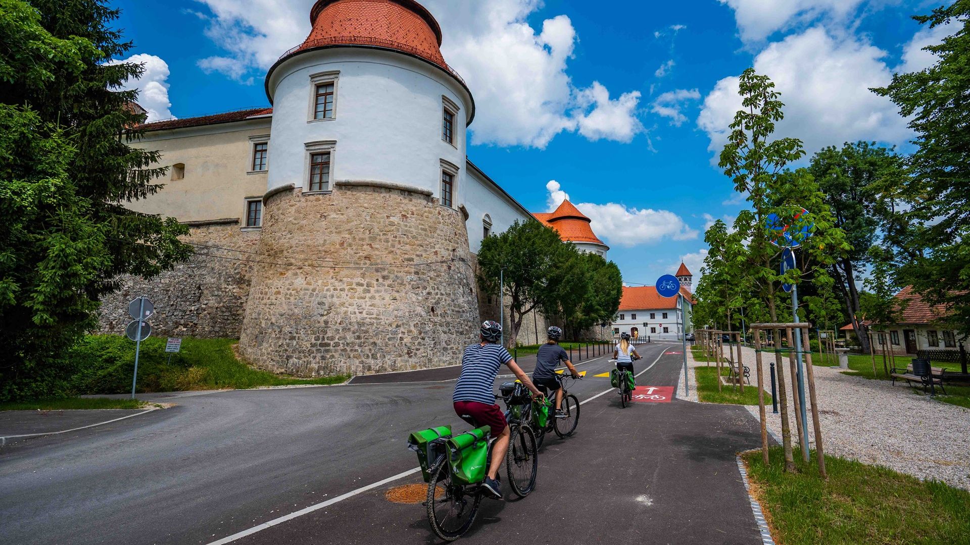 Fotografija treh kolesarjev, ki kolesarijo po cesti, poleg njih grad.