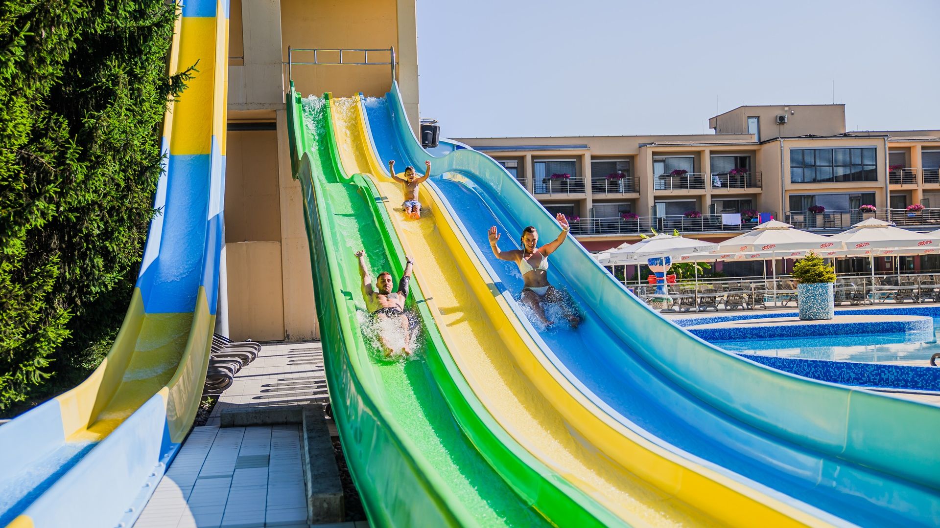 Fotografija družine, ki se spušča po zelenem, rumenem in modrem toboganu v termah.
