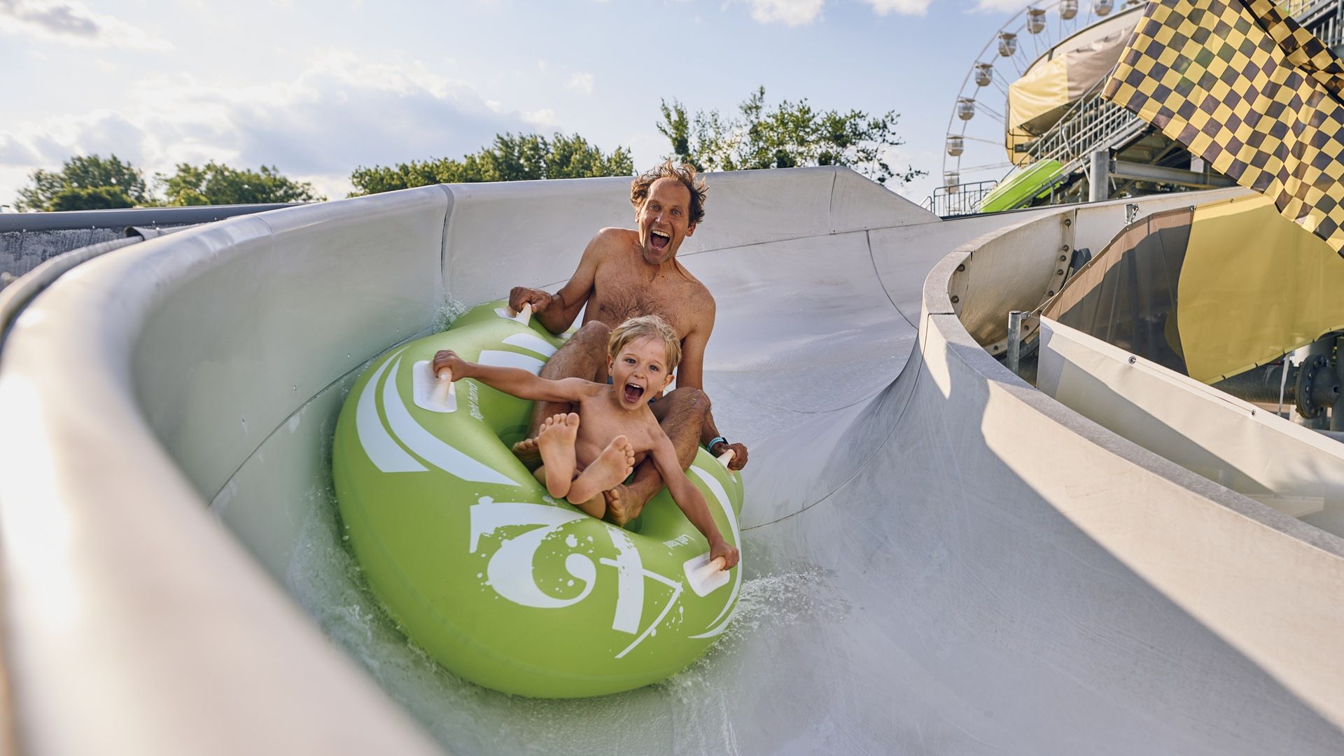 Fotografija očeta in sina, ki se spušča po napihljivem čolnu po vodnem toboganu.