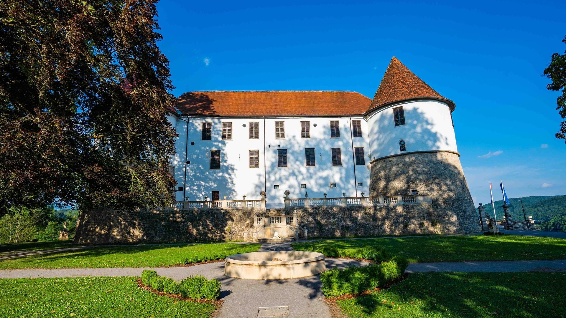 Fotografija gradu Sevnica. Pred njim je zgrajen manjši vodomet.